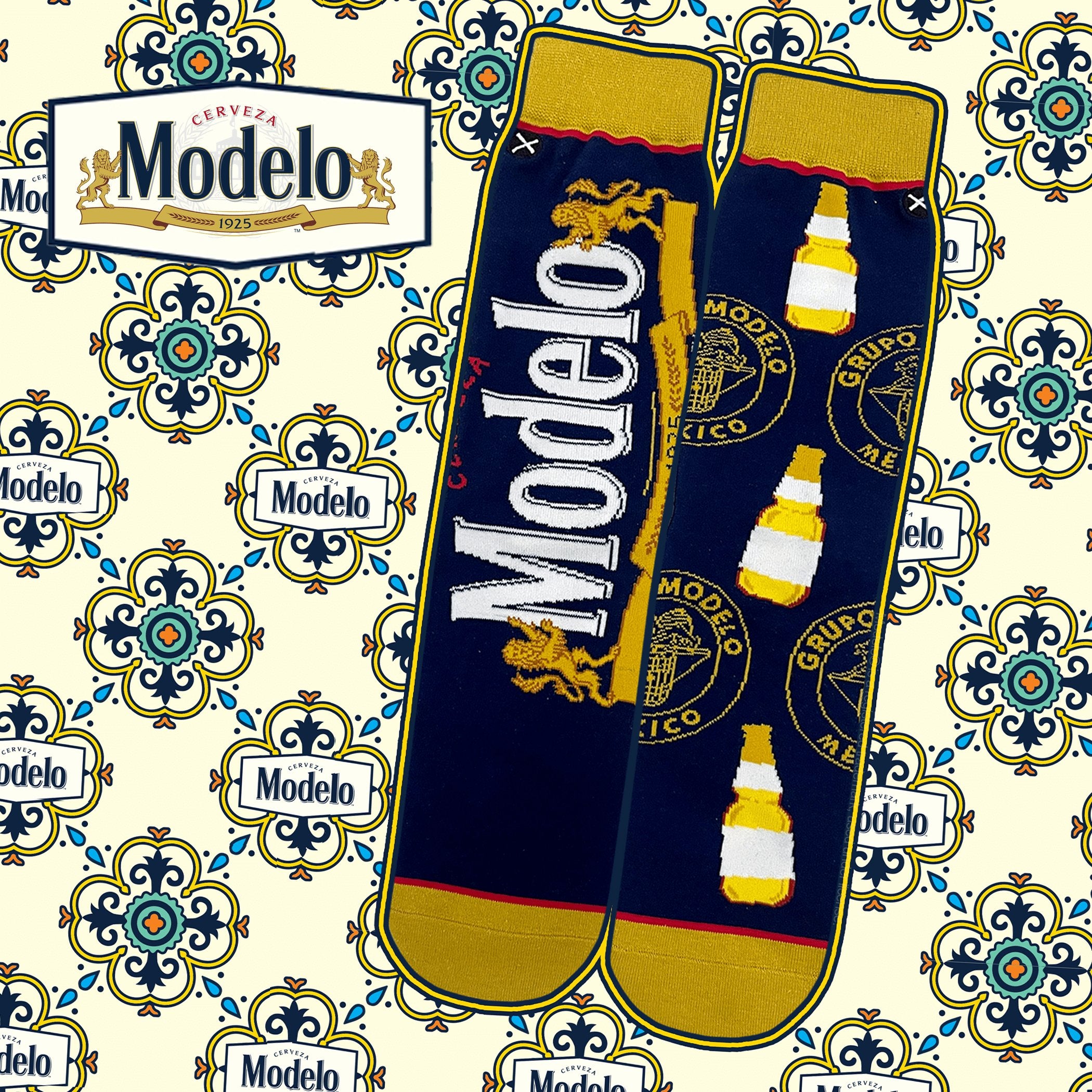 Blue and gold socks with Modelo beer logo and bottle design. Ornate pattern in the background with the Modelo logo in the top left.