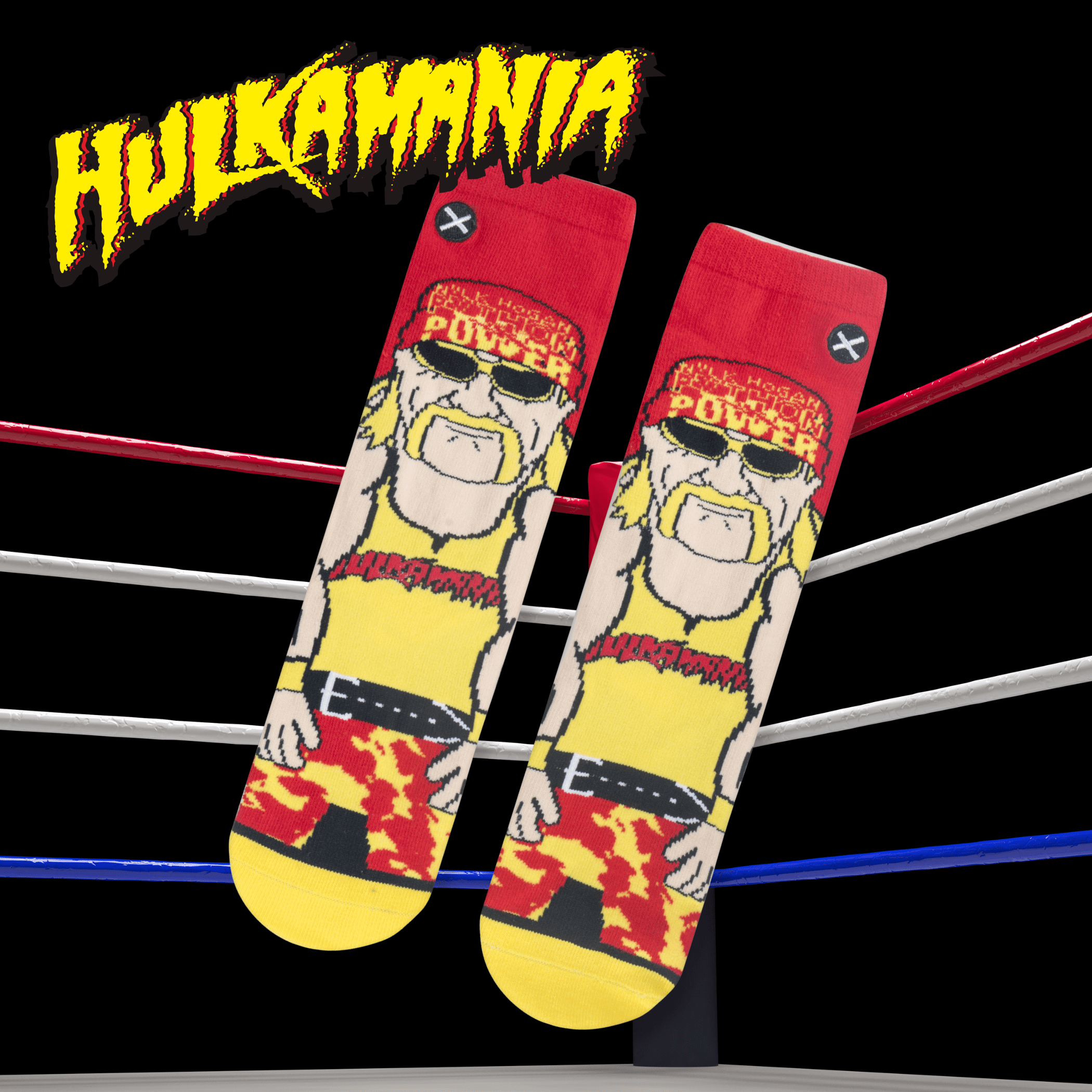 Hulk Hogan-themed socks with a cartoon graphic on a black background, placed inside a wrestling ring with the 'Hulkamania' logo.