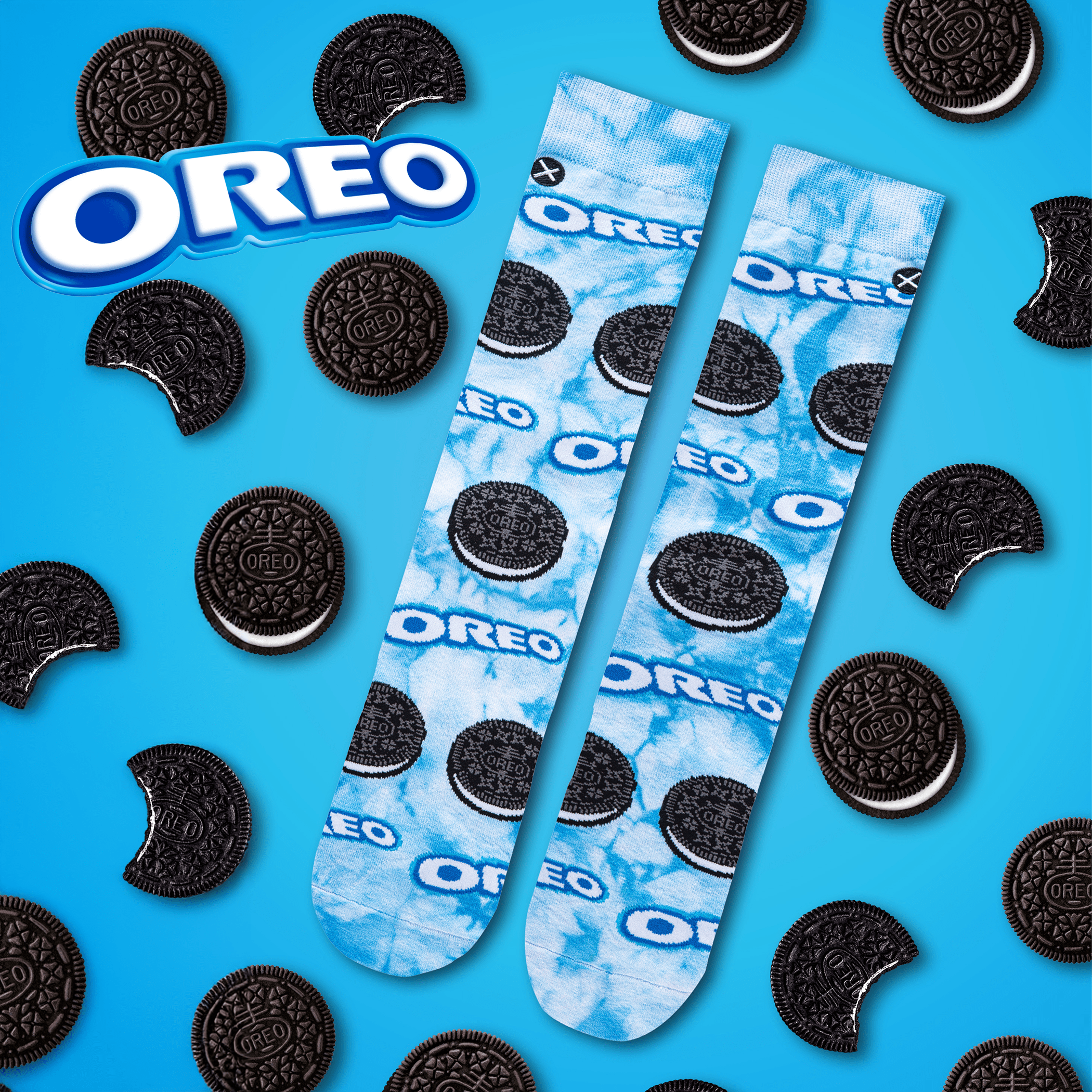Bright blue background with Oreo socks featuring tie-dye patterns and Oreo cookie graphics, surrounded by whole and bitten cookies, representing the beloved cookie snack.