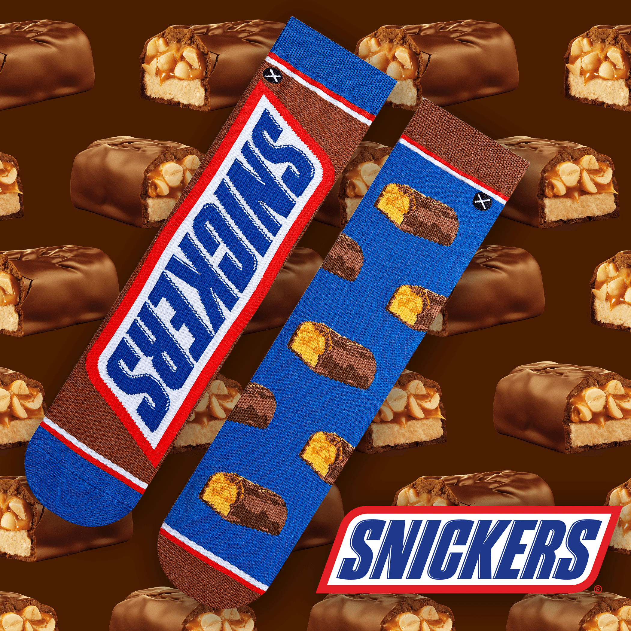 Two socks inspired by Snickers. One has a large Snickers logo, and the other features repeating images of Snickers bars against a blue background. Background shows multiple Snickers bars.