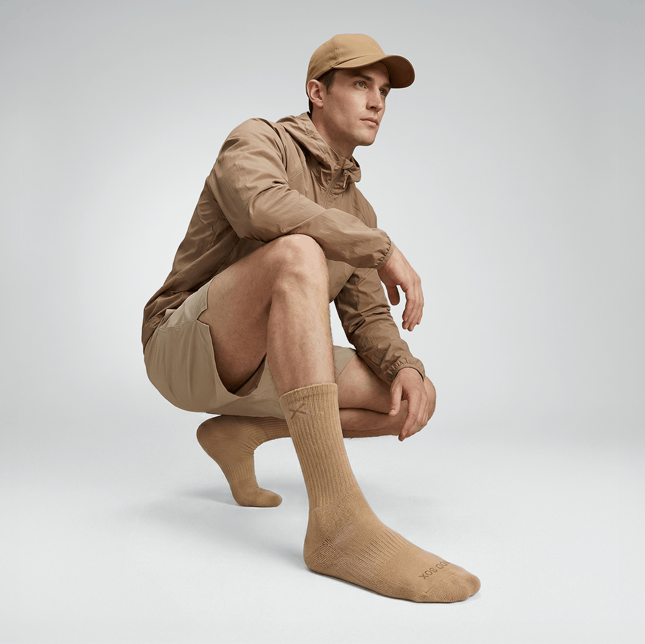 Man wearing a beige outfit with a cap, jacket, and socks on a light gray background