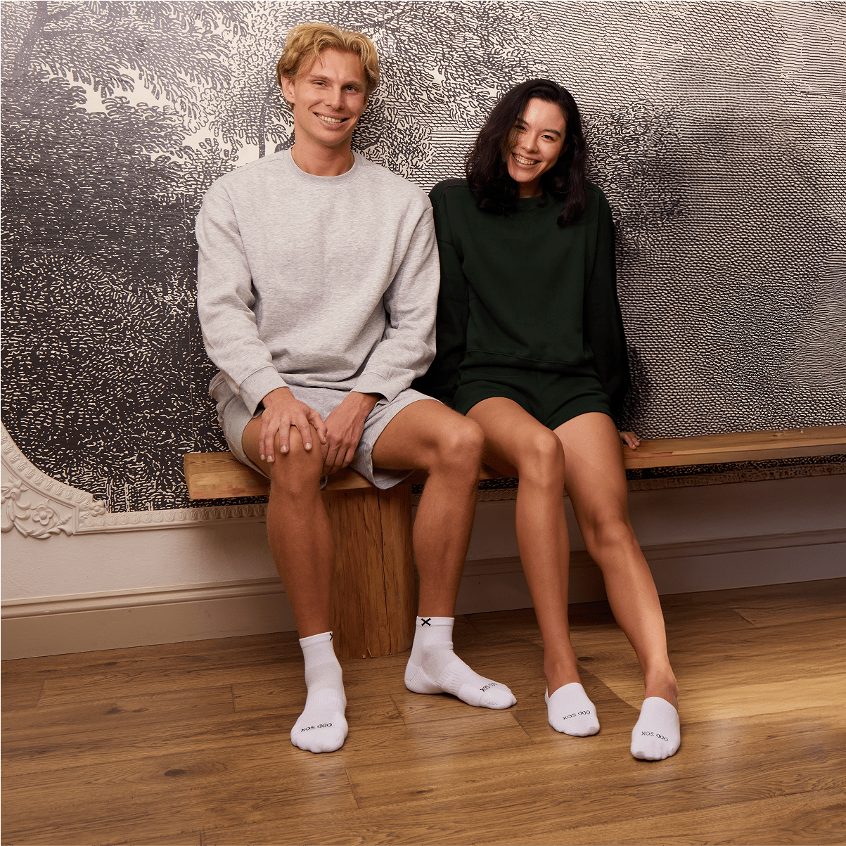 Man and woman sitting on wooden bench wearing casual loungewear and white Odd Sox Basix socks.