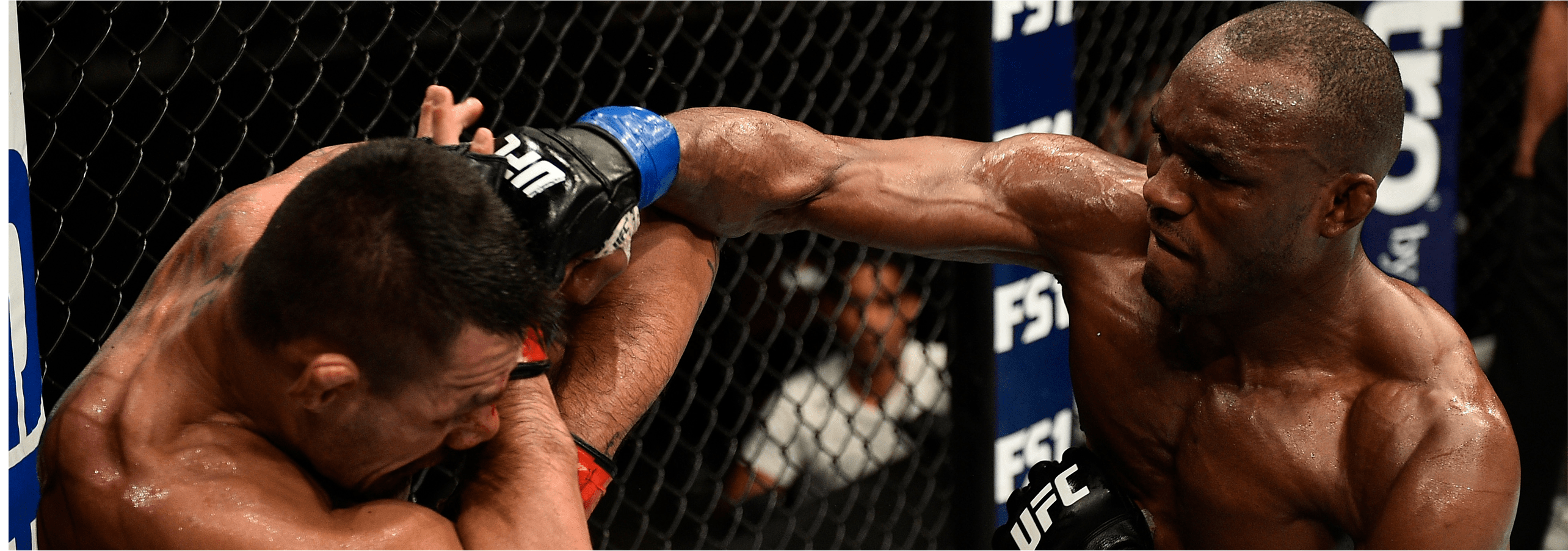 Kamaru Usman lands a strong punch in the clinch during a UFC fight, controlling the action against the cage.