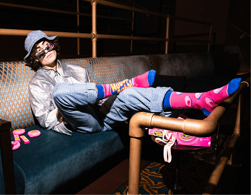 Person sitting on a couch with colorful socks and a hat, surrounded by candy