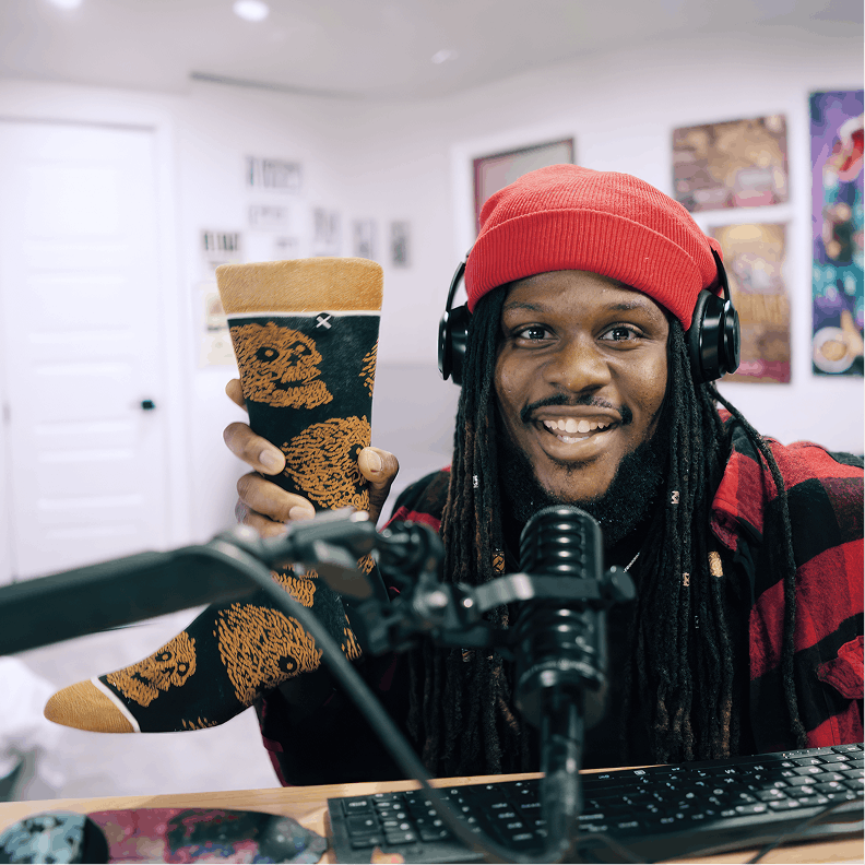 Person holding a coffee cup with a bear design, wearing headphones and sitting in front of a microphone.