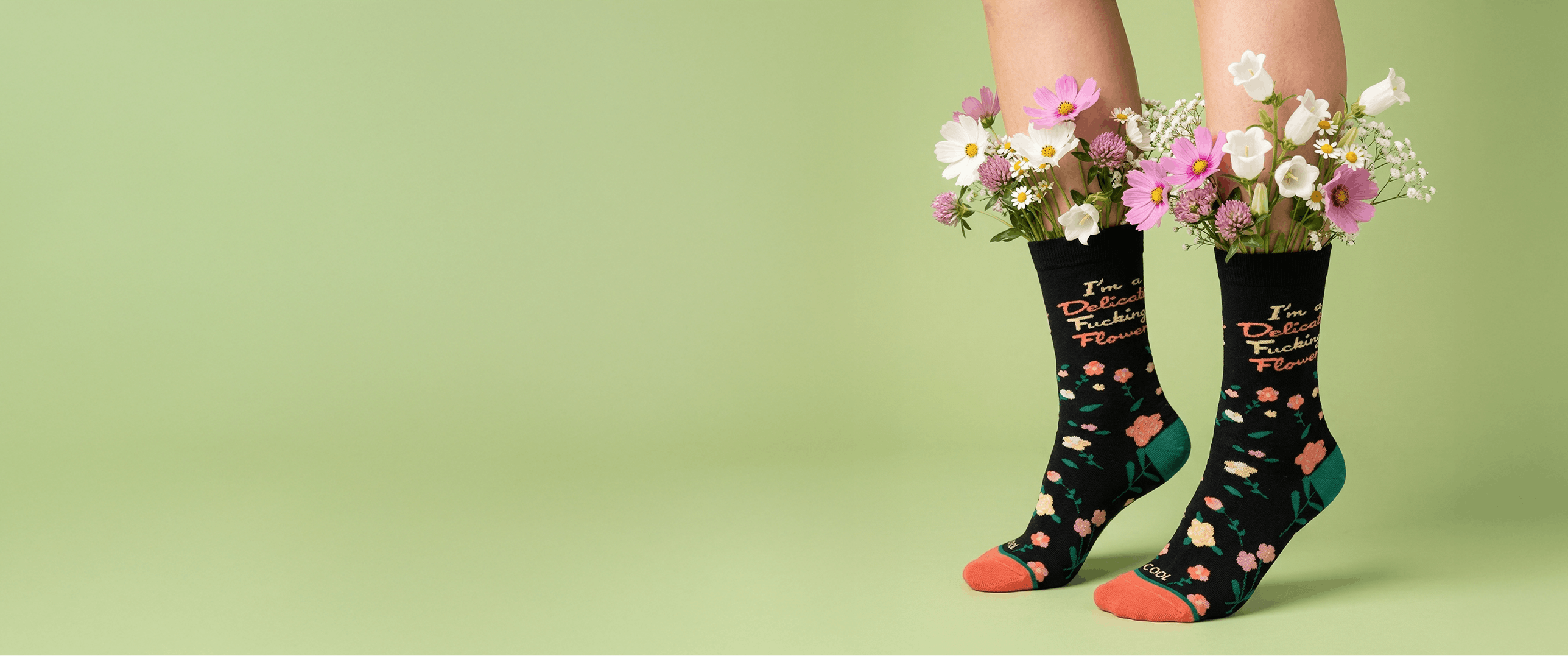 Person wearing socks with floral designs and text, holding flowers against a green background