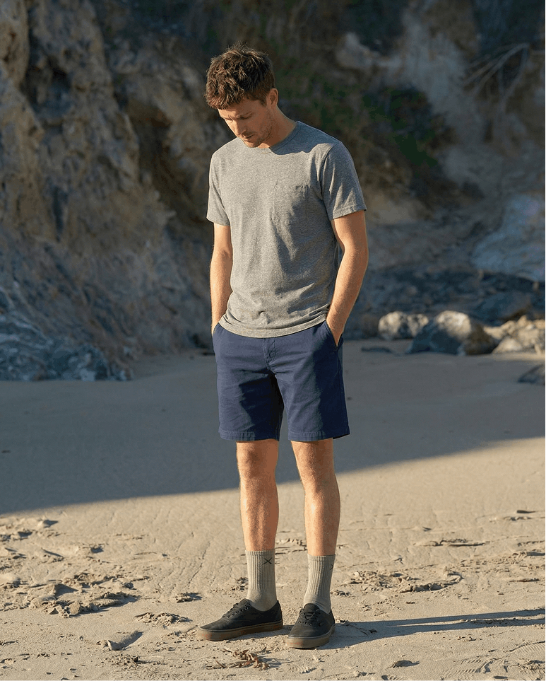 Man standing on a beach wearing a gray t-shirt and blue shorts.