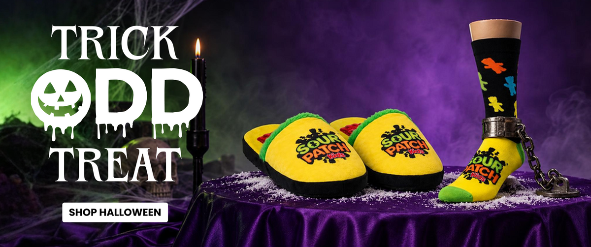 Halloween-themed product display featuring a pair of yellow slip-on slippers and one matching sock with colorful spooky graphics, arranged on a purple draped table with a candle and dark purple background. Large text reads 'TRICK OR TREAT OD TREAT' and 'SHOP HALLOWEEN'.