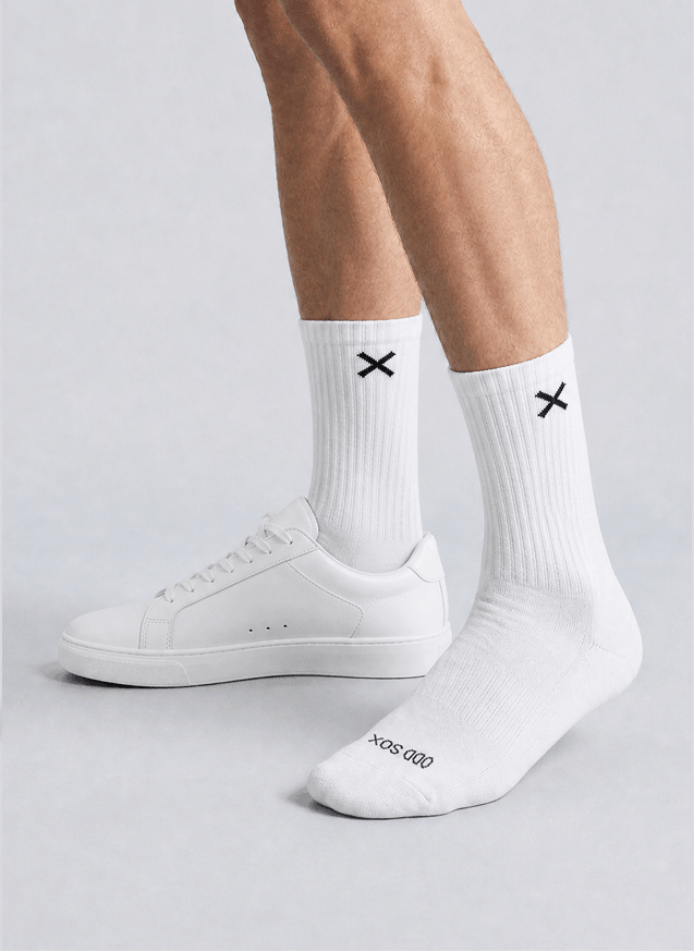 White socks with black X design worn with white sneakers on a light gray background