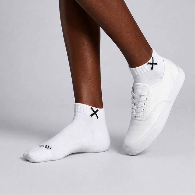 White sneakers and socks with black logo on a neutral background