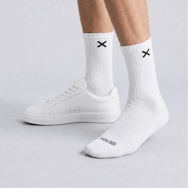 White socks with black 'X' logo worn with white sneakers on a light gray background